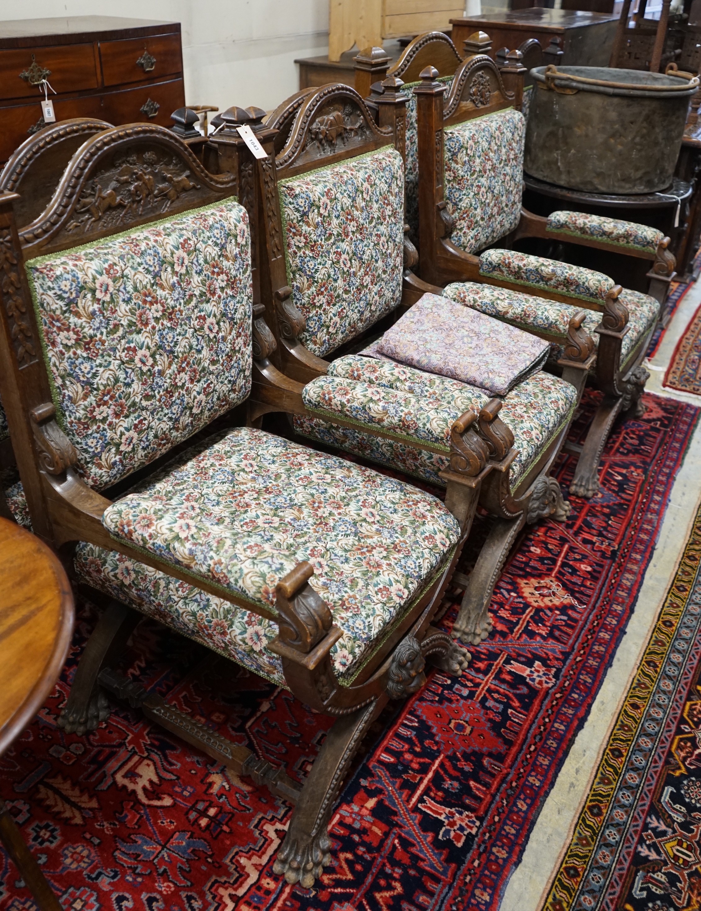 Seven (6+1) early 20th century carved oak upholstered X frame elbow chairs, largest width 75cm, depth 62cm, height 114cm